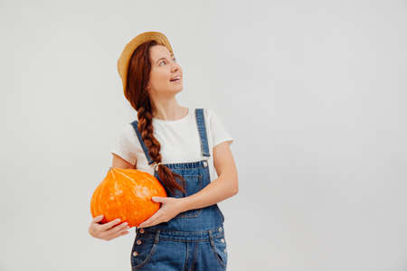 Female village farmer on a white background with a harvest of a large pumpkin. Concept of agriculture and Halloween.の写真素材