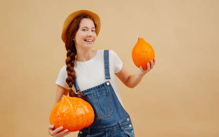 Happy farmer woman in a denim jumpsuit holds ripe pumpkins autumn harvest. Concept of agriculture.の写真素材