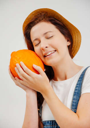 Happy farmer woman in overalls and a hat clutches a ripe little pumpkin. Concept of vegetarianism and oranic food.の写真素材
