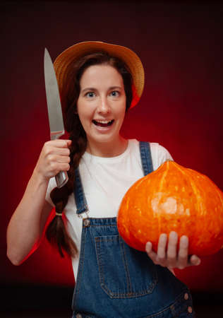 Female gardener aggressively carves a lantern out of a pumpkin with a knife for a horror holiday. Concept of Halloween.の写真素材