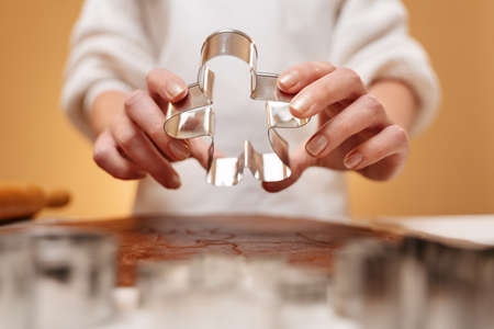 Cooking Christmas gingerbread cookies female hands hold a metal shape in the form of a human body on a yellow background.の写真素材