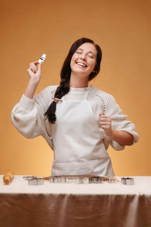 Smiling young woman making dough for baking on yellow background prepares in apron. Concept of gingerbread cookie christmas.の写真素材