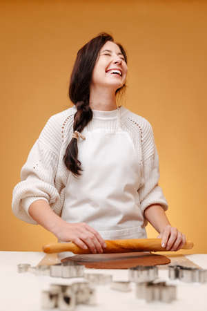 Woman confectioner laughing rolls out the dough for cookies with a wooden rolling pin. Christmas sweets concept.の写真素材