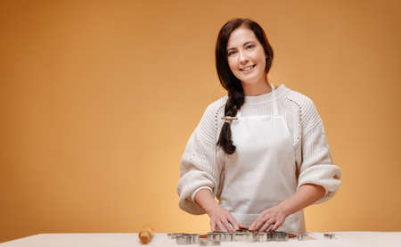 A young woman in a white apron prepares homemade shortbread cookies for Christmas on a yellow background.の写真素材