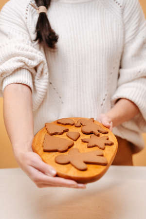 Woman baker in a white sweater holding a wooden board with gingerbread cookies. Concept of food for...