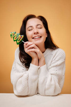 Happy woman portrait on yellow background with green lollipop in the form of a Christmas tree. Healthy smile concept.の写真素材
