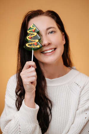 Smiling woman in white sweater holds sweet Christmas tree lollipop candy. Sweet food concept.の写真素材