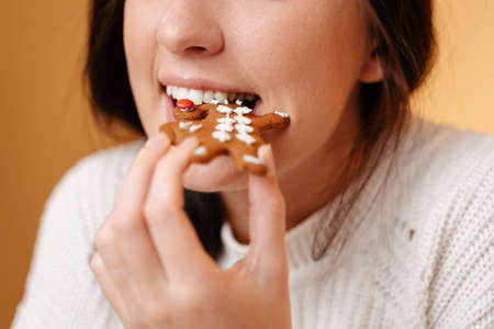Close-up teeth biting off freshly baked gingerbread cookie for christmas. Healthy teeth and sweet concept.の写真素材