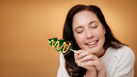 Smiling woman with green lollipop over yellow background. Christmas sweets concept.の写真素材
