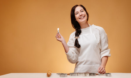 Cheerful woman makes Christmas baking homemade cookies using metal molds on a yellow mold.の写真素材