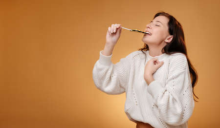 Woman enjoying biting green candy on yellow background. Sweet food concept for christmas.の写真素材