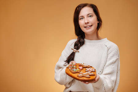 Woman baker in white sweater holds a tray of spicy cookies for Christmas breakfast. Sweet pastry concept.の写真素材