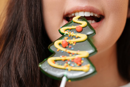 Closeup of green Christmas tree lollipop biting off woman with white healthy teeth. New Years sweets concept.の写真素材