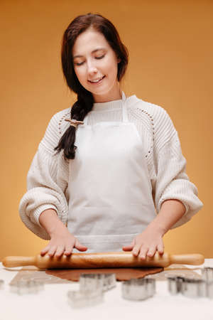 Woman pastry chef rolls out dough for Christmas gingerbread with a rolling pin on a yellow background.の写真素材