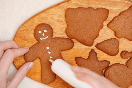 Woman paints on honey gingerbread with white frosting for Christmas breakfast. Confectionery and sweet food concept.の写真素材
