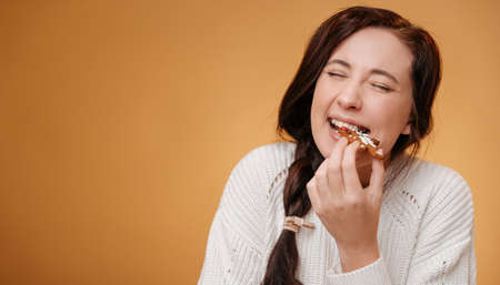 Close-up of a woman biting a gingerbread Christmas cookie on a yellow background. Concept of baking for the new year.の写真素材