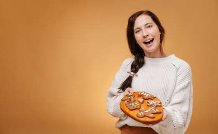 Happy pastry chef woman holding a wooden tray with gingerbread cookies for a traditional holiday christmas on a yellow background.の写真素材
