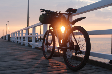 Bicycle with bags is on the pier by the sea, at sunrise. Travel by bike to the sea on a summer morning.の写真素材