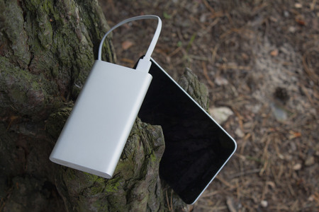 A portable charger charges the Tablet. Power Bank with cable against the background of nature and wood.の写真素材