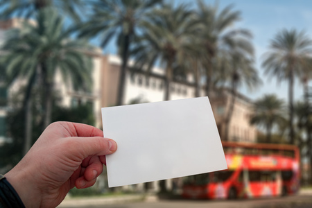 White postcard mockup in man's hand on the background palm trees and travel bus on Mallorca Island in Spainの写真素材