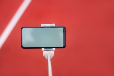 Mock up of a black smartphone with a tripod on the background of the red track for running and sports stadium.の写真素材