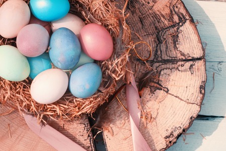 Happy Easter. Colorful Easters eggs in a nest with feathers and a chalk board on a wooden stump