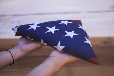 Happy Memorial Day. Girl holds a folded American flag in her hands, on a wooden background.の写真素材