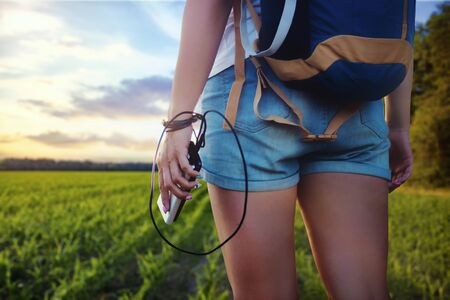 Girl with a backpack on a journey. Tourist holds in her hand a smartphone and a Power Bank on the background of the forest and sunset.の写真素材