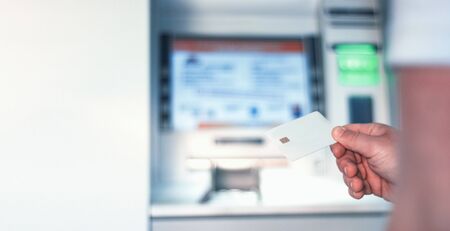A man holds in his hand a mock-up of a white bank card near an ATM.の写真素材