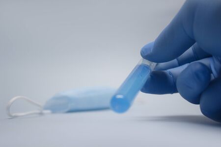 Hand holds glass bottle with Covid-19 coronavirus vaccine against the background of a medical mask....
