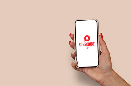 Woman Hand holding the black Mockup smartphone with a close up icon with beautiful nails. Blogger asks to subscribe to his channel for video vlogs. Mobile device isolated on light backgroundの写真素材