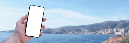 Time to travel. Smartphone in hand, against the background of the sea and the city under a sunny...