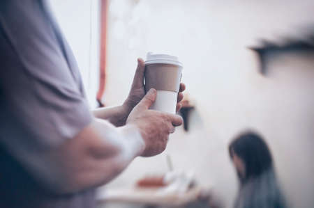 Man holds in his hand a mockup of an ecological paper cup for coffee in a restaurant
