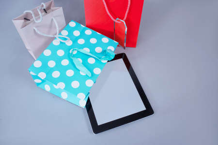Online shopping concept. Close-up tablet mockup with white screen with bright gift bags on gray backgroundの写真素材