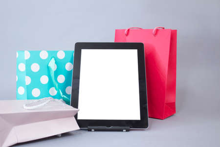 Online shopping concept. Close-up tablet mockup with white screen with bright gift bags on gray backgroundの写真素材