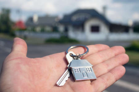 Man holds the keys to the house in his hands against the backdrop of residential buildings. Concept for buying and renting apartments.の写真素材