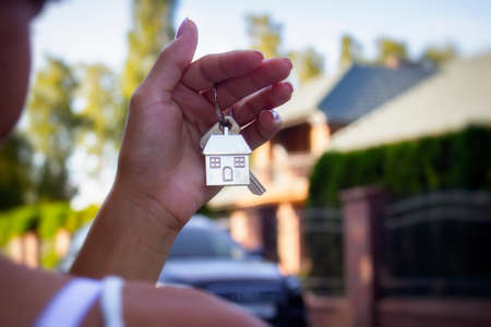A woman holds in her hands the keys to the house against the background of residential buildings and cars. Concept for buying and renting apartments.の写真素材