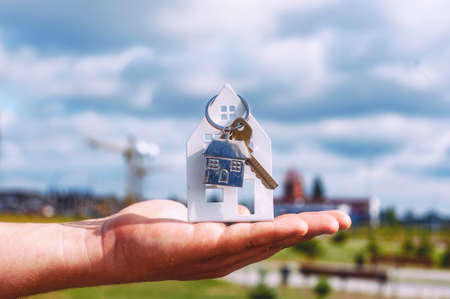 Guy holds the house keys in his hands against the background of clouds. Concept on the topic of buying a new homeの写真素材