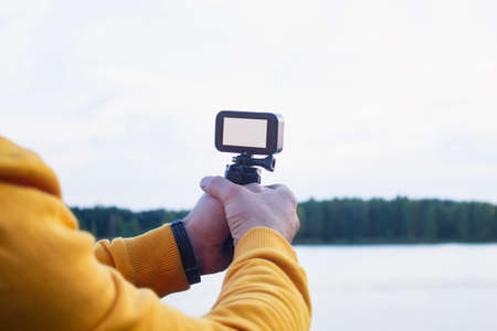 Tourist shoots a video on an action camera against the backdrop of nature and the river. Close-up of a white screen mockup on the camera.の写真素材