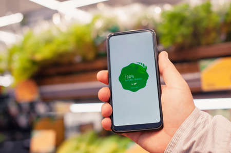 Natural product. A man holds a smartphone in his hands with a label on the screen against the...