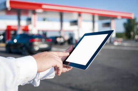 A man holds a close-up of a tablet with a white screen in his hands against the backdrop of a car...