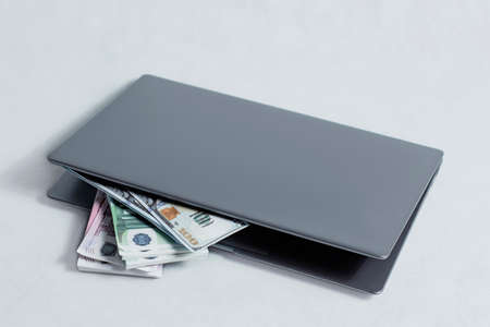 Online work and investment concept. Laptop with a bundle of dollar and euro bills on a white...