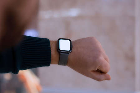 A man with a smartwatch and a white screen mockup on his hand. A man uses a fitness tracker on the...