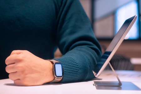 Businessman with digital tablet with white screen on the table and smart watch on his hand. A male freelancer works in a cafeの写真素材