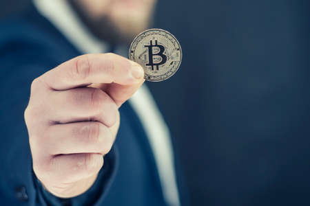 Virtual currency and blockchain concept. Businessman in a blue jacket holding Bitcoin in his hands