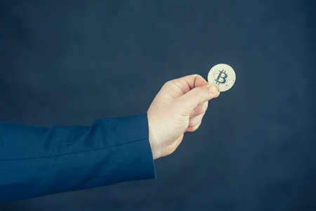 Virtual currency and blockchain concept. Businessman in a blue jacket holding Bitcoin in his hands