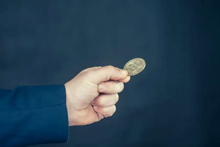 Virtual currency and blockchain concept. Businessman in a blue jacket holding Bitcoin in his hands