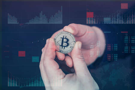 Businessman holds a gold bitcoin coin in his hands. Information holographic panel with statistics...