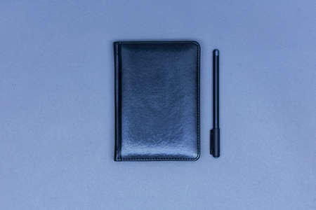 A closed black leather notebook lies on the table with a pen for notesの写真素材