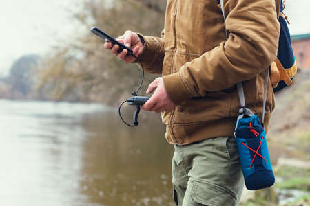Tourist holds a portable charger with a smartphone in his hand. A man on the background of a lake with a backpack charges the telephone with Power Bank. Concept on the theme of tourismの写真素材